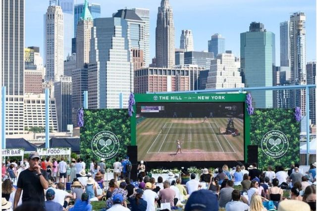 A crowd watching tennis on a large screen outdoors